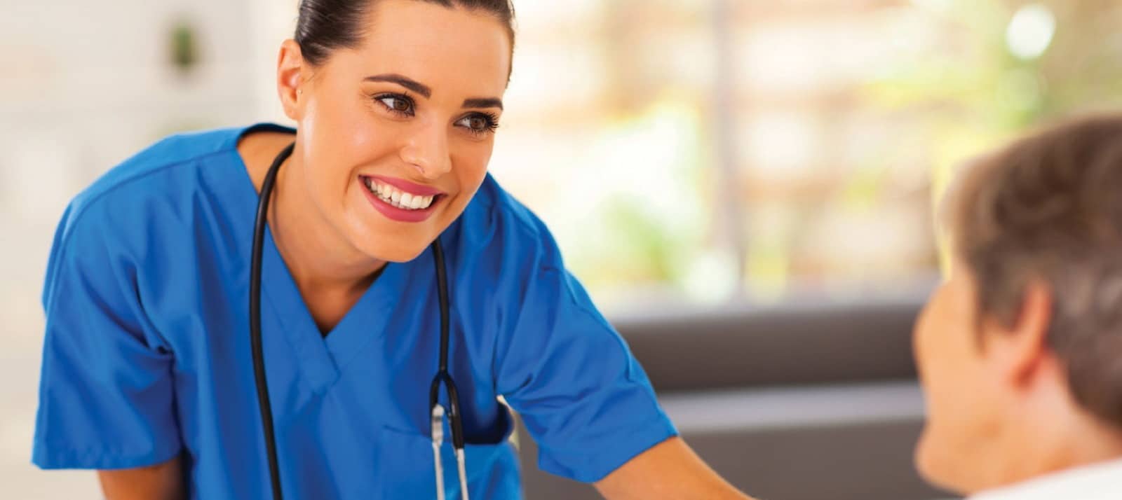 אישה עם סטטוסקופ על הצוואר רוכנת למטופל שיושב